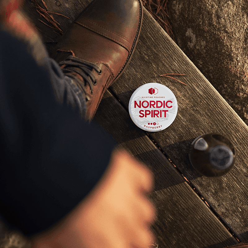 Lifestyle shot showing a can of Nordic Spirit Raspberry Nicotine pouches by a mans boot on a wooden step.