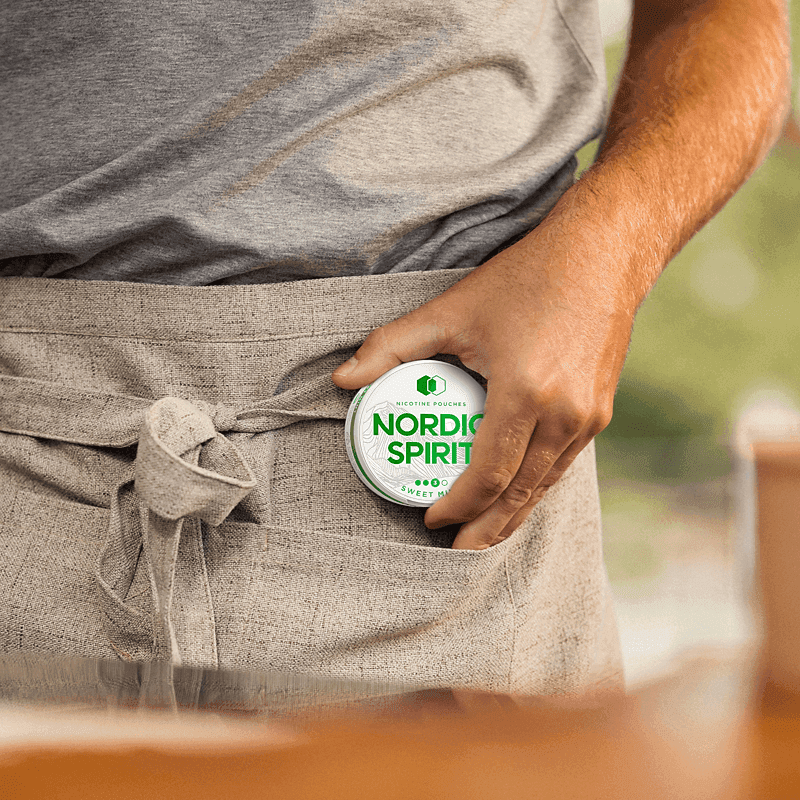 Lifestyle shot of a man placing a can of Nordic Spirit Sweet Mint Strong Nicotine Pouches in his apron pocket.
